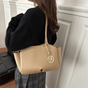 Beige faux leather tote bag with M metal tag carried by a model in casual setting