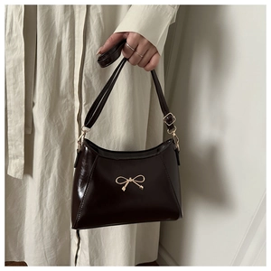 Close-up of a dark brown patent leather handbag with a golden metal bow decoration