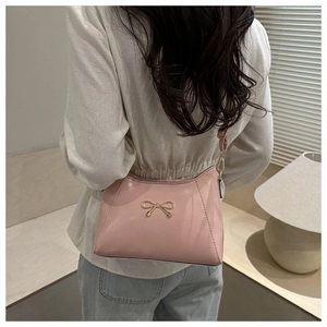 Detail of pink shoulder bag featuring a golden bow accent and smooth faux leather finish