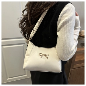Detail of white PU leather shoulder bag featuring a decorative gold bow metal buckle