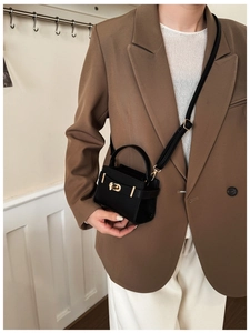 Petit sac en cuir noir avec boucle dorée porté sur un blazer marron style élégant chic