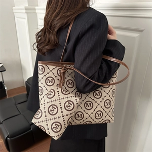 Chic beige canvas tote bag with M logo pattern and leather trim shown in a modern interior
