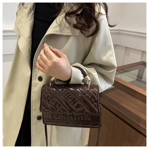 Detail of dark brown patent leather handbag with embossed fashion lettering on model