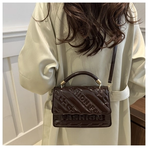 Detail of chocolate patent leather bag with embossed letters worn by a model
