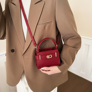 Mini sac Kelly rouge en cuir grainé avec détails dorés porté par un mannequin