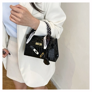 Detail of crocodile pattern texture on black patent leather bag with gold buckle
