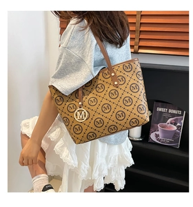 Détail du sac cabas en cuir marron avec motif 'M' répétitif et breloque en métal gravée