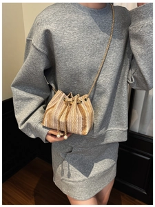 Close-up of a woven straw bucket bag with gold chain strap and elegant pearl charms