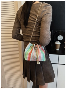 Detail of colorful woven bucket bag with gold chain strap and pearl drawstring charm