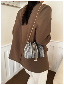 Detail of woven bucket bag with elegant pearl drawstring charms and gold chain strap