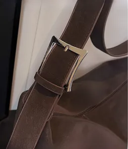 Détail macro de la boucle en métal argenté poli et de la bandoulière en cuir marron mat