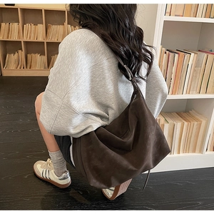 Sac cabas en daim marron avec bandoulière réglable dans un décor de bibliothèque