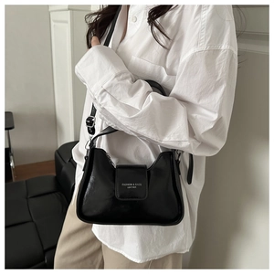 Detail of minimalist black glossy leather crescent bag worn as a stylish crossbody bag