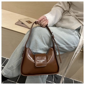 Detail showing the dark brown leather texture and printed logo on the minimalist shoulder bag