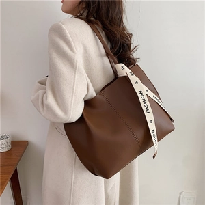 Brown leather tote bag with FASHION decorative strap, worn with a white coat