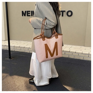 Detail of pink woven tote bag with large brown leather M letter and premium leather trim