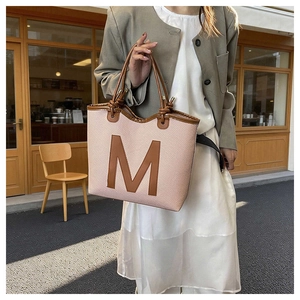 Detail of pink woven tote bag featuring a large brown leather M and knotted handles