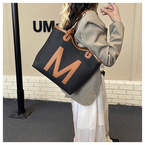 Detail view of large tote bag featuring a textured black fabric and brown leather M patch