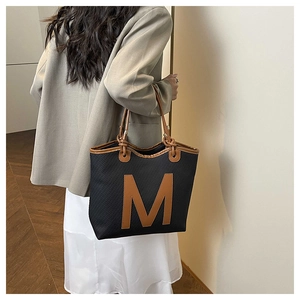 Detail of large black tote bag with brown M logo and vertical striped fabric texture