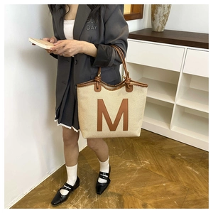 Detail of woven tote bag with brown leather M patch and stylish rope knot handle