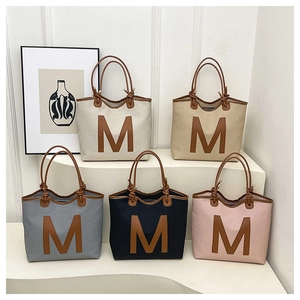 Detail of woven tote bags showing large M leather logo and fine knitted texture in five colors