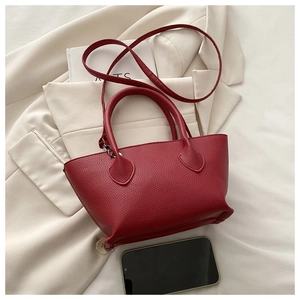 Detail of red pebble leather handbag showing top handles, shoulder strap and silver hardware