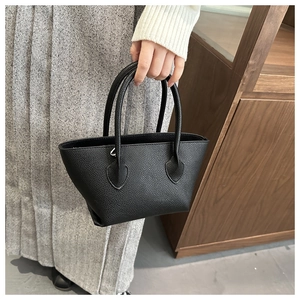 Detail of black pebbled leather tote bag with sturdy handles held by a model
