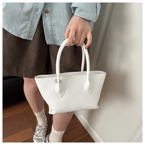 White pebbled leather tote bag with silver hardware held by a model in casual outfit