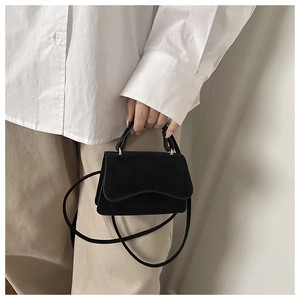 Detail of minimalist matte black leather handbag with wavy flap and adjustable strap