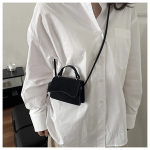 Detail of a black suede mini crossbody bag with a wave-pattern flap and shoulder strap