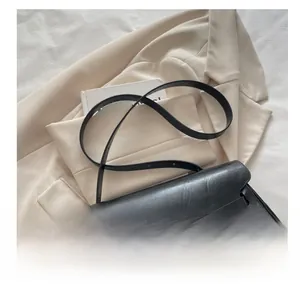 Detail view of black matte leather shoulder bag with adjustable strap on a beige blazer