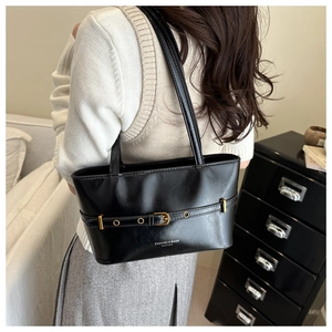 Chic black glossy leather tote bag with gold buckle detail shown on female model