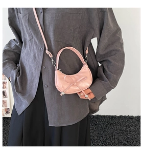 Pink patent leather crescent bag featuring a delicate bow knot and adjustable strap detail