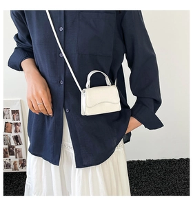 Detailed view of a white mini crossbody bag featuring a unique wavy flap and top handle