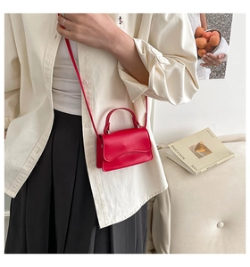 Detailed view of red mini shoulder bag with wavy edge flap and top handle on a model