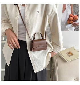Detail of a brown leather mini crossbody bag with unique wavy stitching and top handle