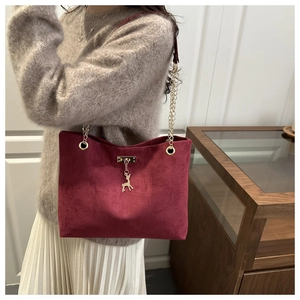Detail of burgundy suede tote bag featuring a gold deer charm and metallic chain strap