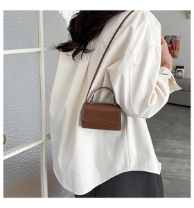 Detailed view of a dark brown mini leather crossbody bag shown on a model for scale