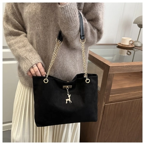 Detail of black suede tote bag featuring golden chain straps and a delicate deer pendant