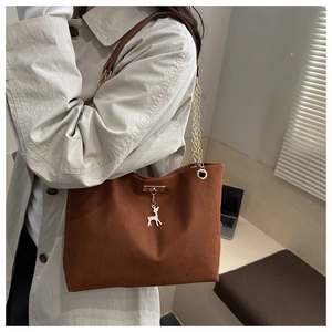 Detail view of dark brown canvas tote bag featuring a gold chain strap and metal deer pendant