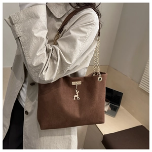 Detail of a brown suede tote bag with gold deer pendant and chain strap on shoulder