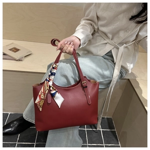 Detailed shot of a red leather tote bag featuring a vintage print silk scarf on the handle