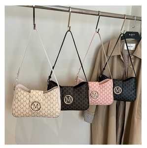 Detail view of four shoulder bags with M-pattern print and gold logo hanging on a rack