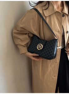 Close-up of vintage monogram shoulder bag with gold M-logo buckle on a beige coat