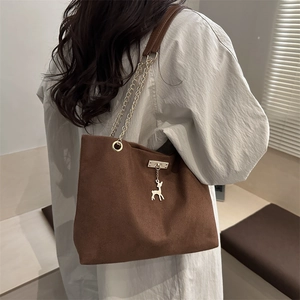 Retro brown suede tote bag with gold chain strap and deer pendant in a soft interior setting