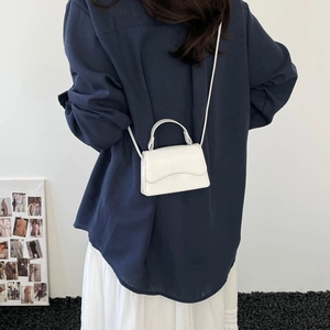 Minimalist white micro crossbody bag with a wave-edged flap and semi-circular handle