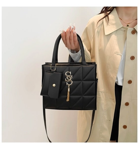 Détail d'un sac à main noir matelassé avec logo doré, pompon et mini porte-monnaie