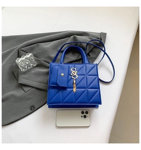 Detail of royal blue quilted handbag with gold SS logo, tassel, and mini pouch
