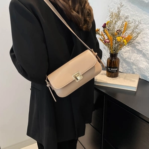 Sac à bandoulière beige minimaliste avec boucle dorée porté sur un blazer noir