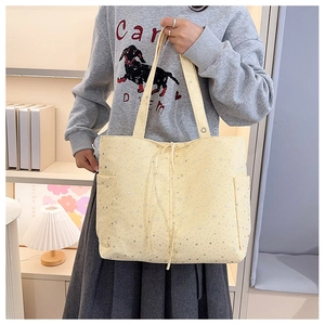 Detalle de bolso tote de lona amarillo claro con estrellas plateadas y bolsillos